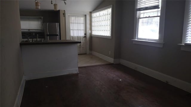 kitchen with kitchen peninsula, stainless steel fridge, hardwood / wood-style flooring, sink, and lofted ceiling