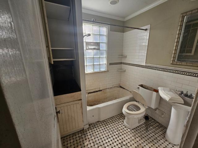 bathroom featuring tile walls, toilet, tile floors, tiled shower / bath combo, and ornamental molding