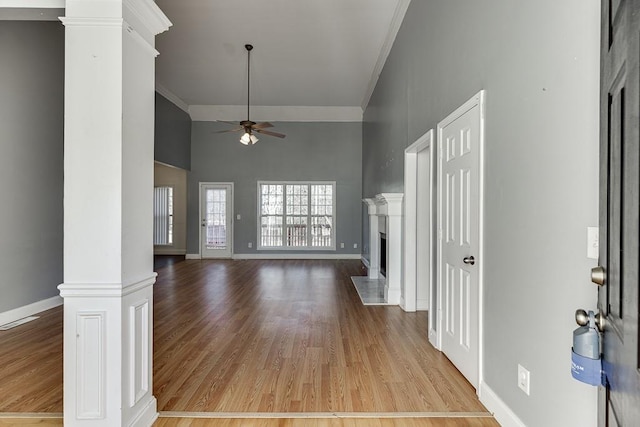 unfurnished living room with a towering ceiling, ornate columns, light hardwood / wood-style floors, ceiling fan, and crown molding