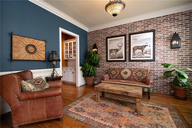 sitting room featuring brick wall, crown molding, wood finished floors, wainscoting, and an accent wall