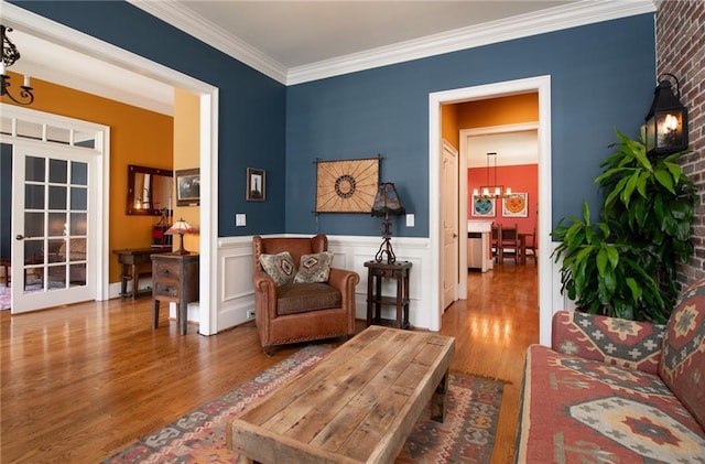 sitting room with a chandelier, wood finished floors, crown molding, and wainscoting
