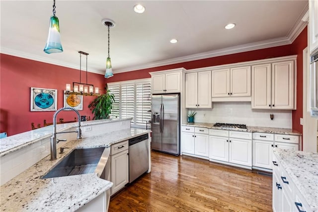 kitchen featuring stainless steel appliances, a sink, hanging light fixtures, white cabinets, and ornamental molding