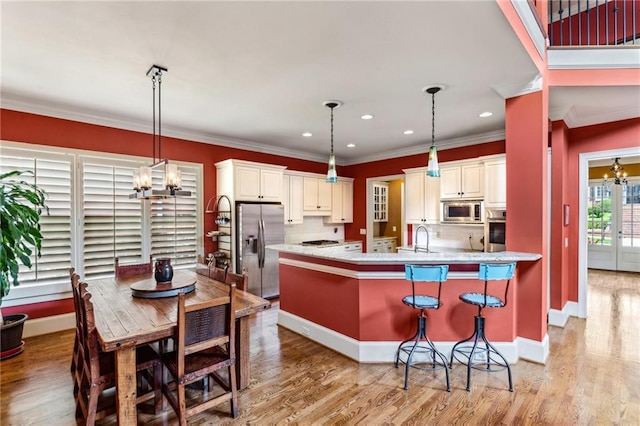 kitchen featuring stainless steel appliances, a chandelier, ornamental molding, a kitchen breakfast bar, and hanging light fixtures