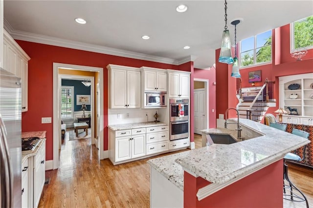 kitchen with appliances with stainless steel finishes, a sink, healthy amount of natural light, white cabinets, and crown molding