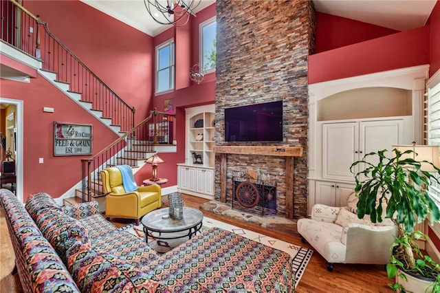 living area with a high ceiling, wood finished floors, a fireplace, stairs, and a chandelier