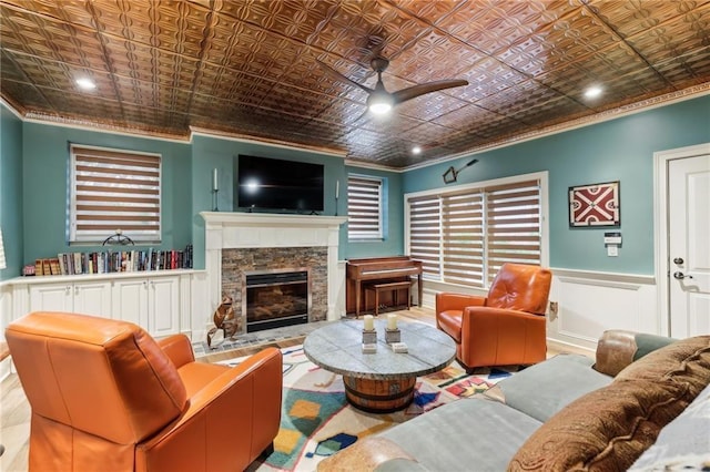 living area featuring an ornate ceiling, ceiling fan, crown molding, a fireplace, and wainscoting