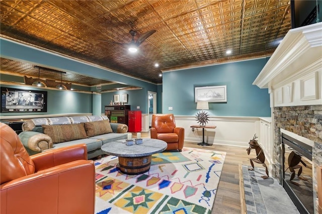 living room featuring ornamental molding, a stone fireplace, wood finished floors, a wainscoted wall, and an ornate ceiling