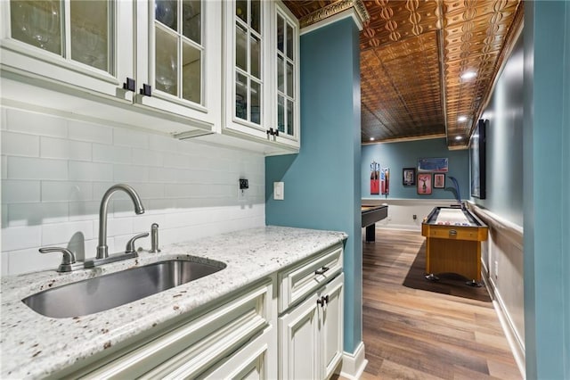 kitchen with a sink, billiards table, light stone counters, backsplash, and glass insert cabinets