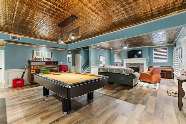 recreation room with an ornate ceiling, ornamental molding, wood finished floors, a stone fireplace, and billiards table