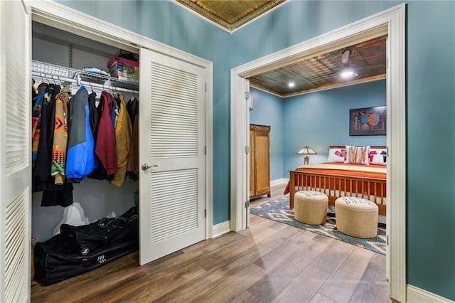 bedroom with ornamental molding, a closet, wood finished floors, baseboards, and an ornate ceiling