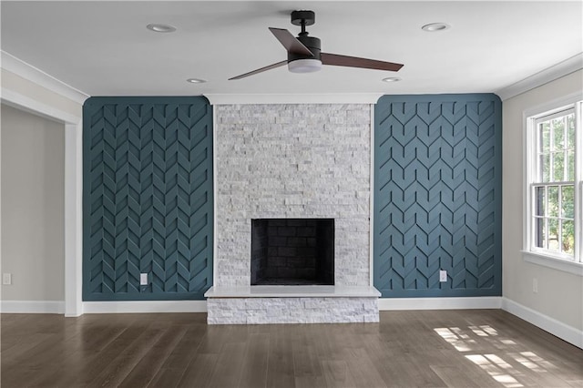 unfurnished living room featuring an accent wall, a stone fireplace, dark wood-type flooring, and crown molding