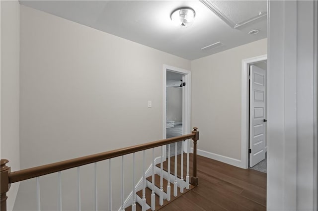 hallway with baseboards, visible vents, dark wood finished floors, and an upstairs landing