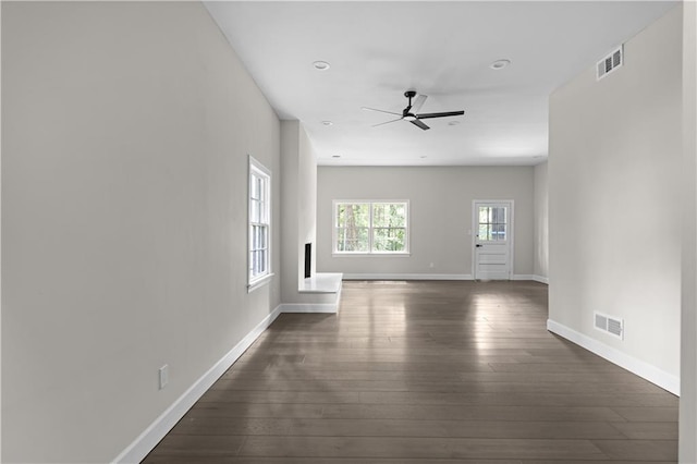 unfurnished living room featuring dark wood-type flooring, visible vents, baseboards, and a ceiling fan