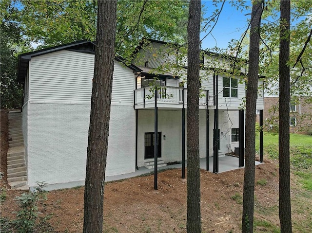 back of house with a balcony, brick siding, and a patio