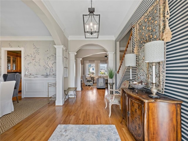 foyer entrance with decorative columns, crown molding, a notable chandelier, and light hardwood / wood-style flooring