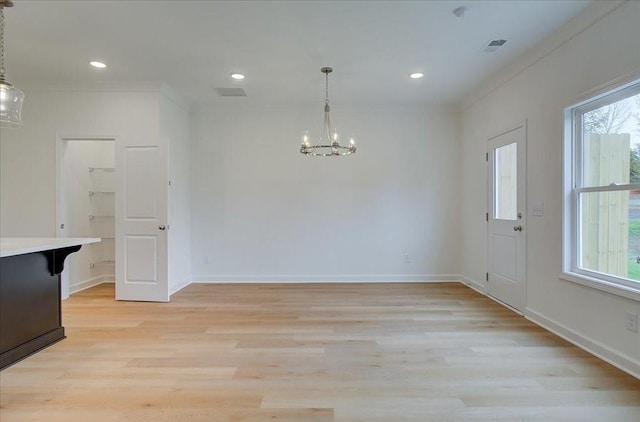 unfurnished dining area with crown molding, an inviting chandelier, and light wood-type flooring