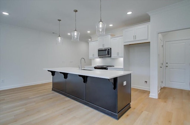 kitchen featuring pendant lighting, sink, a kitchen island with sink, light hardwood / wood-style floors, and white cabinets