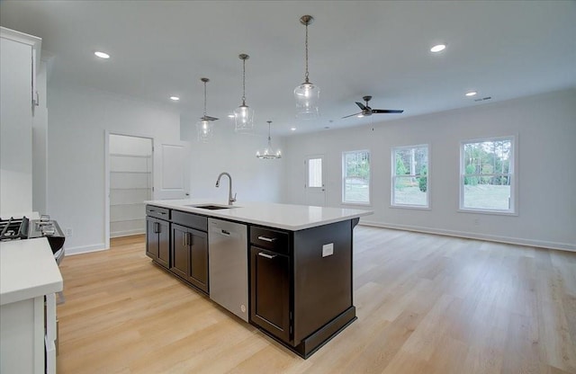 kitchen featuring decorative light fixtures, dishwasher, sink, a kitchen island with sink, and light wood-type flooring