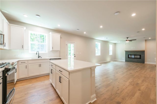 138 Henley St, Canton, GA 30114 - kitchen featuring a sink, stainless steel gas stove, ceiling fan, a glass covered fireplace, and a kitchen island