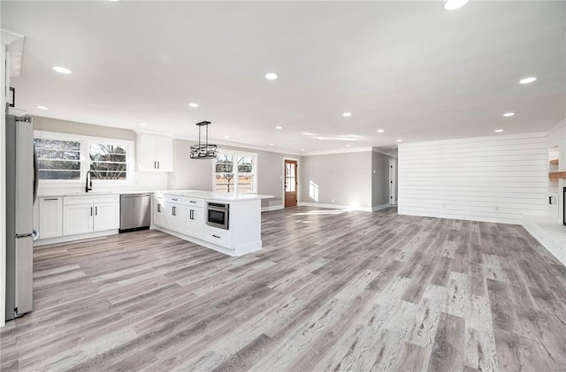 kitchen featuring appliances with stainless steel finishes, a peninsula, open floor plan, light wood-style floors, and recessed lighting