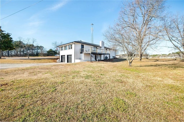 rear view of house featuring a garage, a wooden deck, driveway, a chimney, and a yard