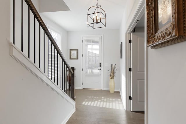 foyer entrance featuring baseboards, a notable chandelier, wood finished floors, and stairway