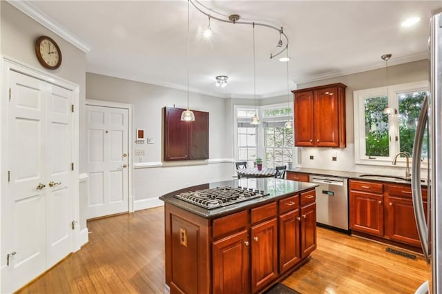 kitchen with light wood-style flooring, appliances with stainless steel finishes, dark countertops, a sink, and a center island