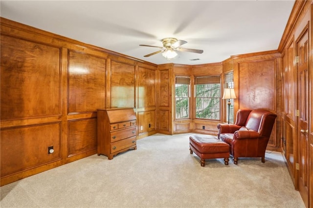 living area featuring wood walls, ceiling fan, ornamental molding, and light carpet