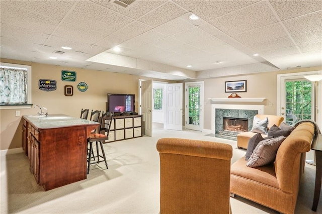 living room featuring light colored carpet, a healthy amount of sunlight, baseboards, a drop ceiling, and a premium fireplace