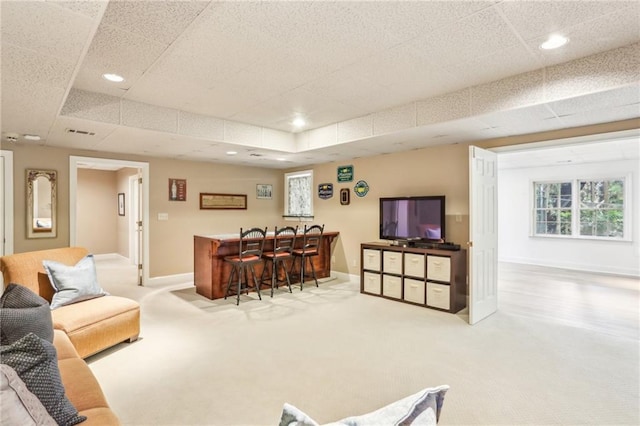 carpeted living area featuring indoor bar, visible vents, a drop ceiling, and baseboards