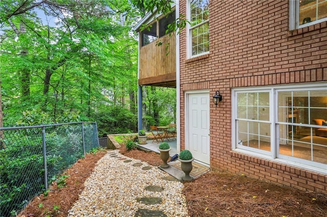 view of exterior entry featuring brick siding, fence, a balcony, and a patio area