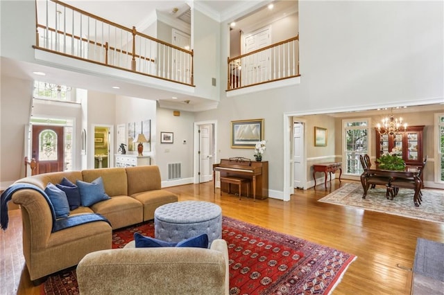 living area with wood finished floors, a notable chandelier, a high ceiling, and crown molding