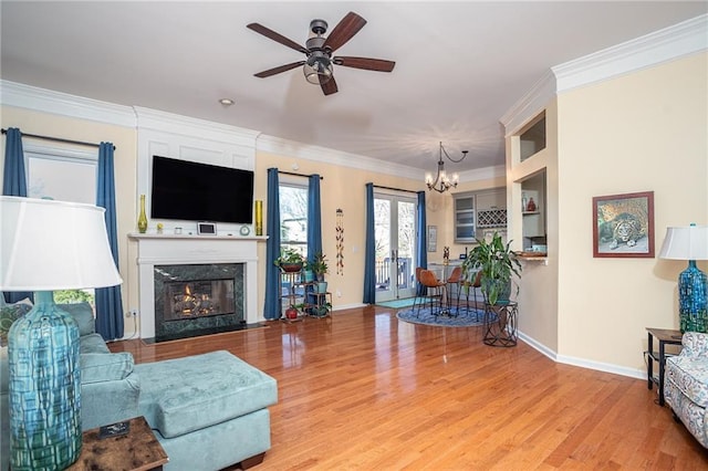 living area featuring ornamental molding, ceiling fan with notable chandelier, wood finished floors, a fireplace, and baseboards