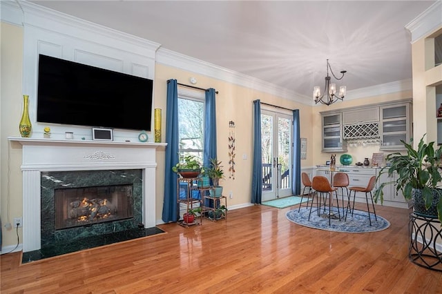 living room with a chandelier, ornamental molding, a high end fireplace, and wood finished floors