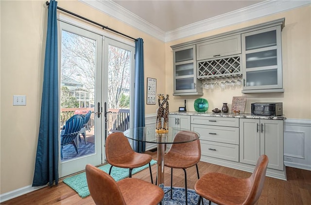 dining space featuring wood finished floors, baseboards, ornamental molding, french doors, and a dry bar