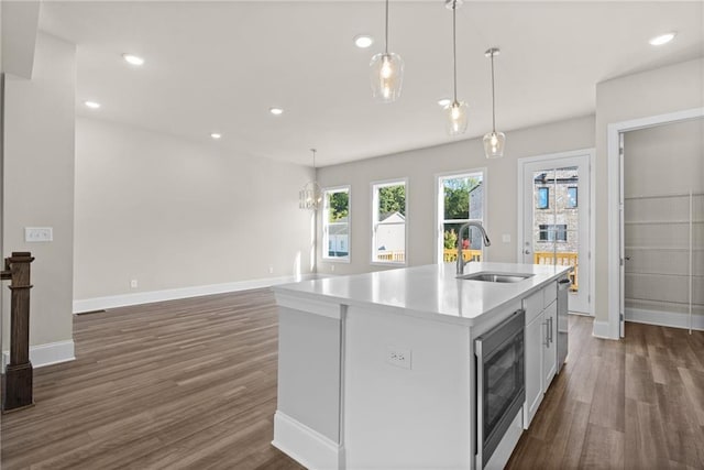 kitchen featuring dark hardwood / wood-style flooring, sink, a center island with sink, white cabinetry, and hanging light fixtures