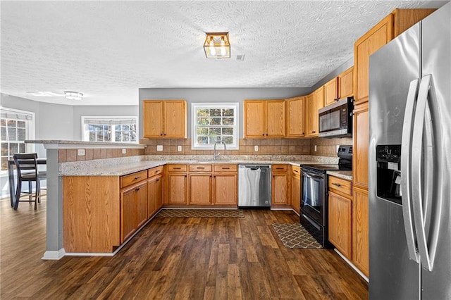 kitchen featuring kitchen peninsula, appliances with stainless steel finishes, dark hardwood / wood-style flooring, decorative backsplash, and light stone countertops