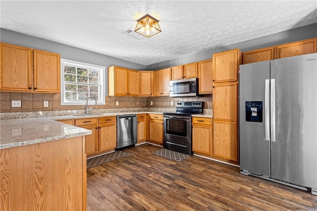 kitchen featuring light stone countertops, appliances with stainless steel finishes, dark hardwood / wood-style flooring, backsplash, and sink