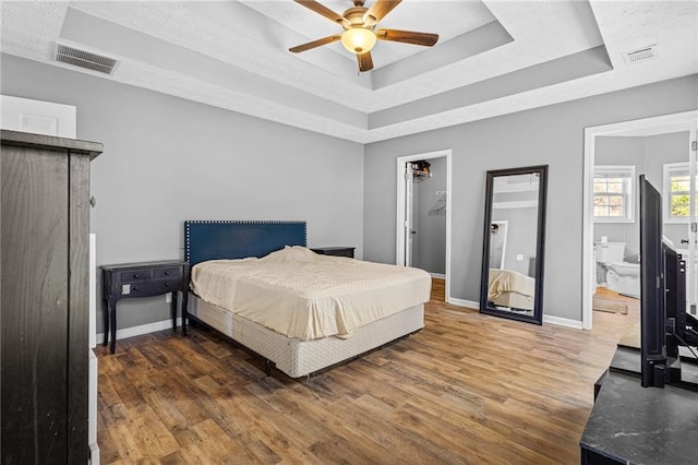 bedroom with ensuite bath, a tray ceiling, ceiling fan, a spacious closet, and dark hardwood / wood-style floors