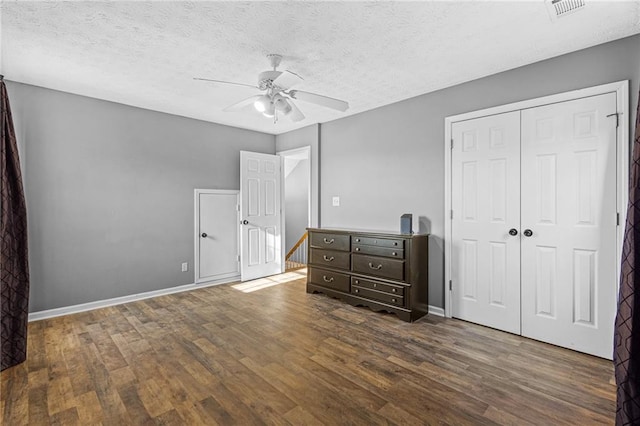 unfurnished bedroom featuring a textured ceiling, dark hardwood / wood-style flooring, a closet, and ceiling fan