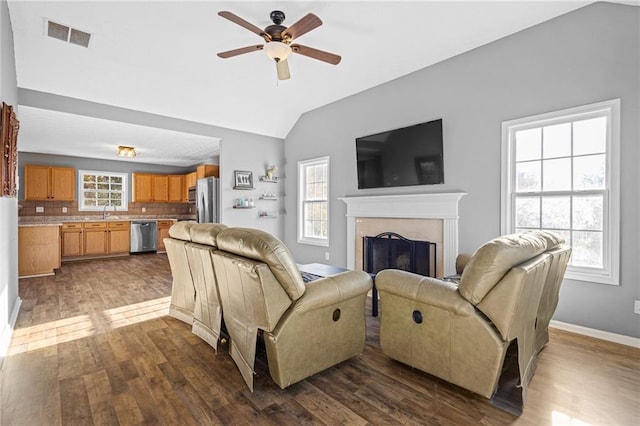 living room with a high end fireplace, ceiling fan, dark wood-type flooring, sink, and lofted ceiling