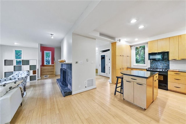 kitchen with light hardwood / wood-style floors, decorative backsplash, light brown cabinetry, a kitchen island, and black appliances