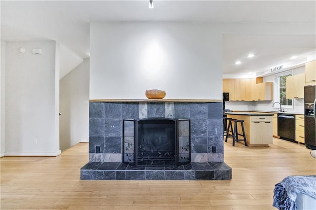 interior details featuring black appliances, a tiled fireplace, sink, and hardwood / wood-style floors