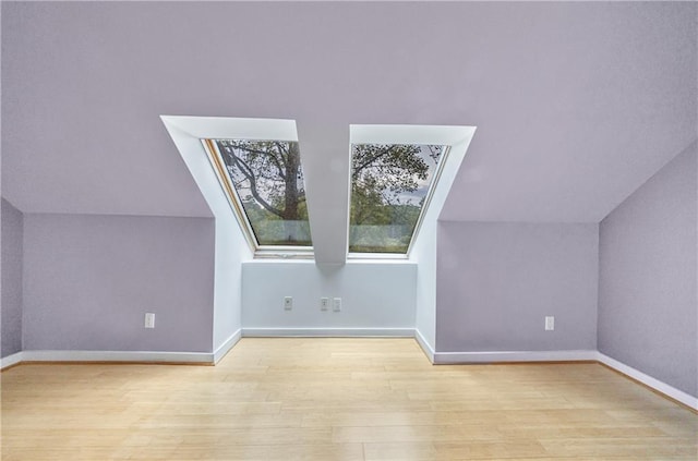 additional living space featuring light hardwood / wood-style flooring and lofted ceiling with skylight