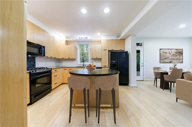 kitchen with light brown cabinetry, light wood-type flooring, a kitchen island, and black appliances