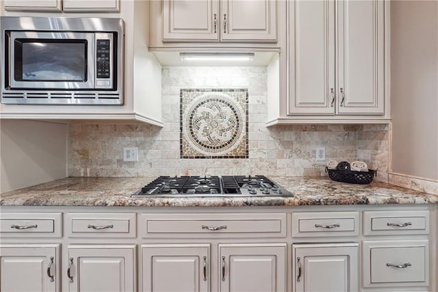 kitchen with light stone countertops, stainless steel appliances, tasteful backsplash, and white cabinetry