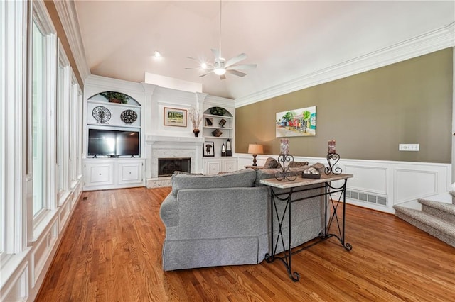 living room featuring vaulted ceiling, light hardwood / wood-style flooring, crown molding, ceiling fan, and built in features