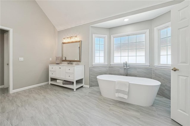 bathroom featuring vanity, a bathing tub, vaulted ceiling, and tile walls