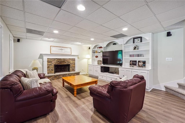 living room featuring a stone fireplace, a paneled ceiling, and light hardwood / wood-style floors