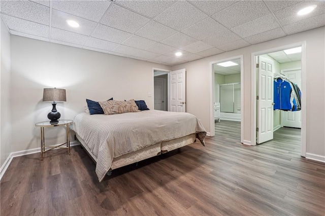 bedroom with dark wood-type flooring, a closet, a drop ceiling, a walk in closet, and ensuite bath